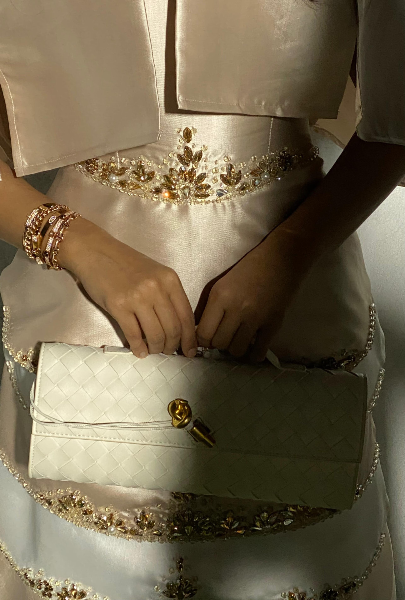 An ivory gown with gold embellishment and a white woven clutch